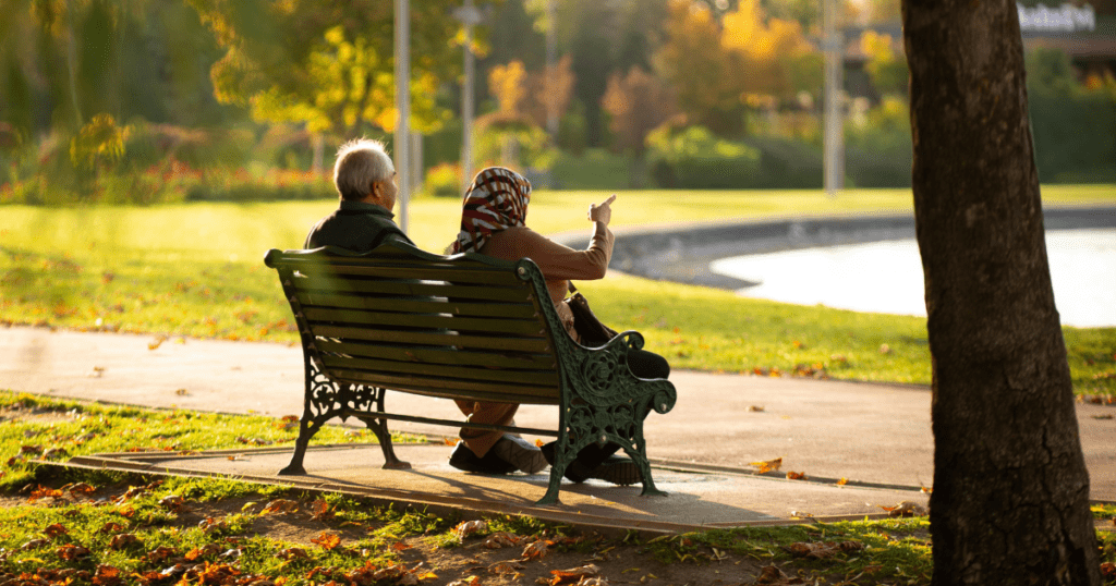 High earning couple enjoying retirement on a park bench in autumn, representing the financial freedom lifestyle goal from building wealth early
